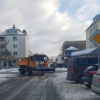 Zaśnieżone ulice, samochody z czapami śniegu na maskach, maszyny odśnieżające śnieg z ulic, chodników
