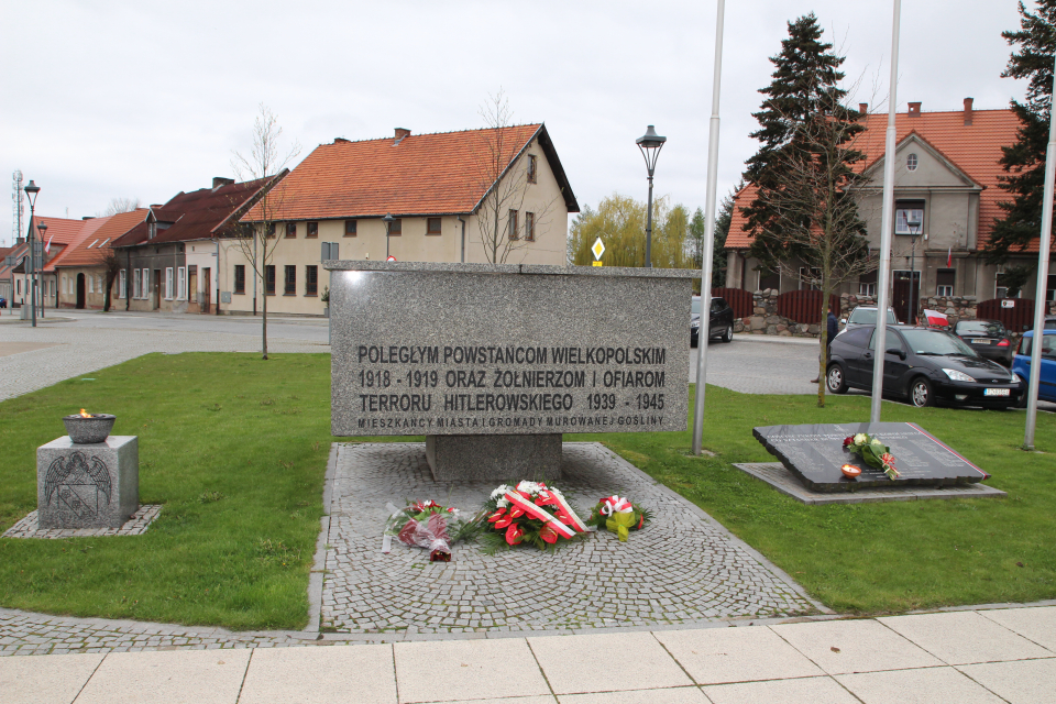 Zdjecie - płonący znicz i wiązanki kwiatów pod pomnikiem na placu Powstańców Wlkp. w Murowanej Goślinie