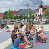 Publiczność siedząca na placu. W tle kamienice i ratusz miejski.