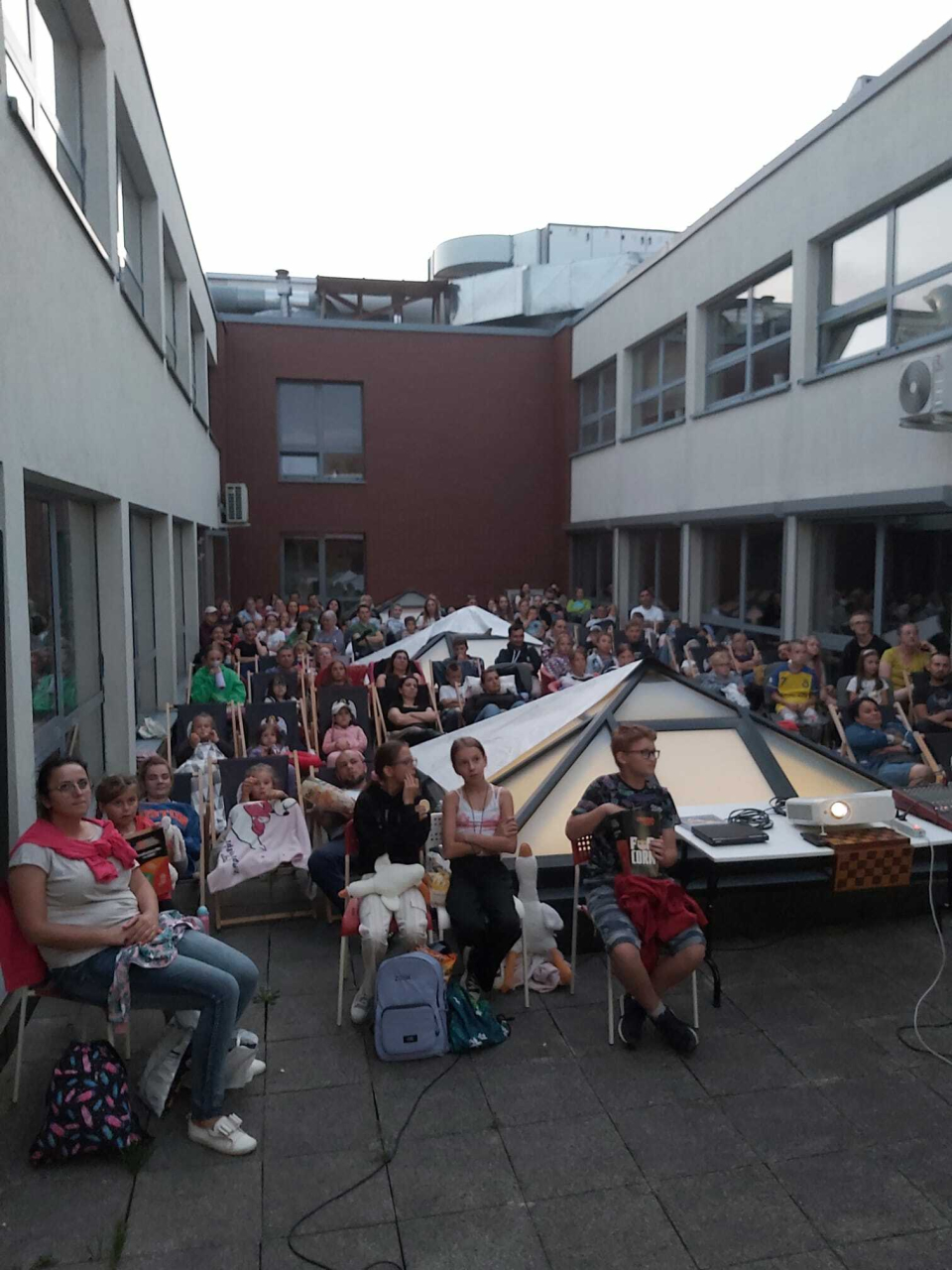widzowie siedzący na leżakach i ławkach, na dachu budynku