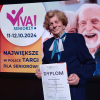 kobieta z dyplomem na scenie, w tle ekran z napisem Viva Wielkopolski Senior Konkurs Wielkopolska Otwarta na Osoby Starsze