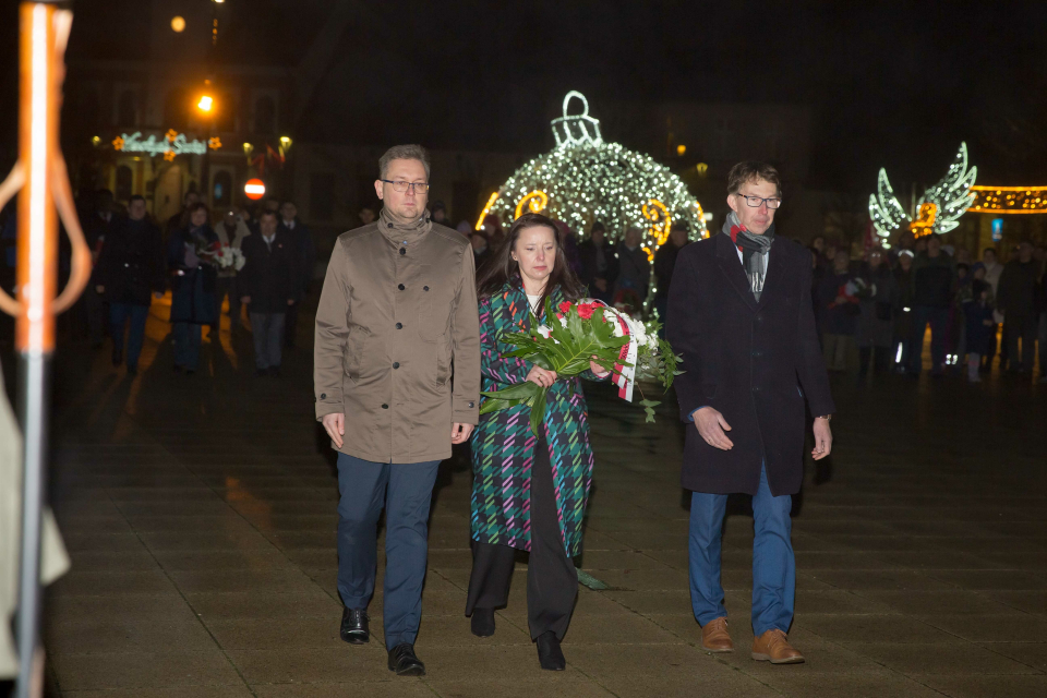 kobieta i dwóch mężczyzn niesie wiązankę kwiatów