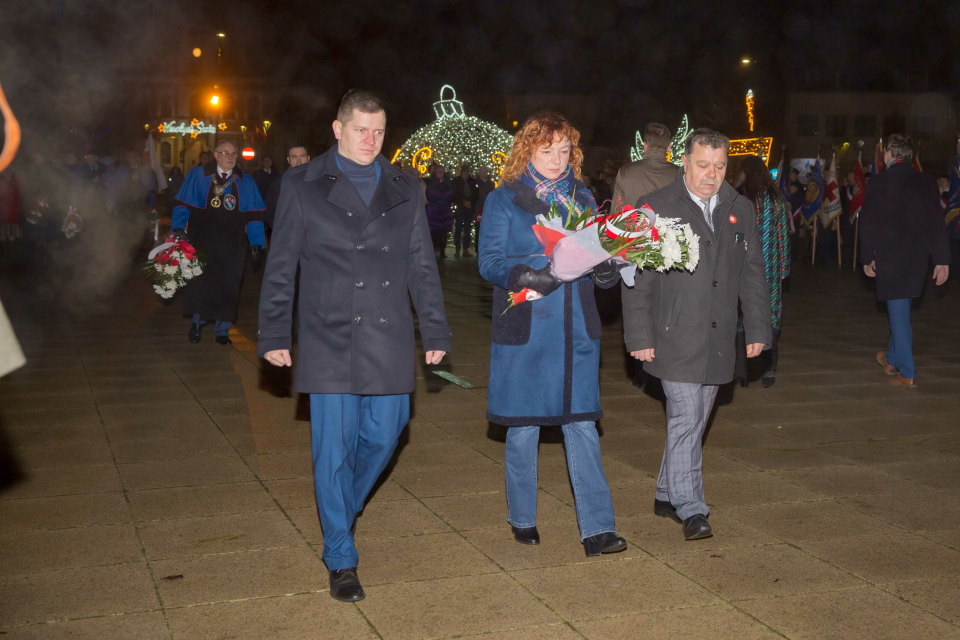 kobieta i dwóch mężczyzn niesie wiązankę kwiatów