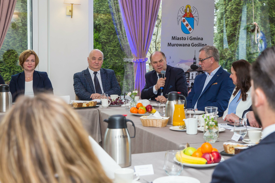 ludzie siedzą przy stole, mężczyzna trzyma mikrofon