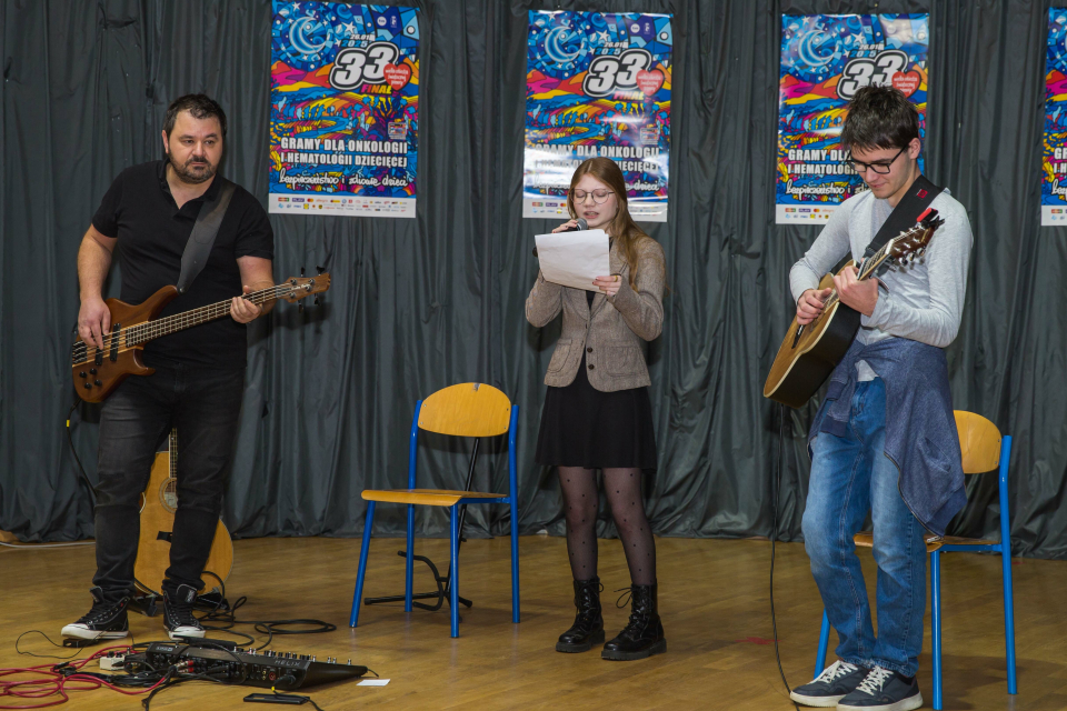 dwóch mężczyzn z gitarami i kobieta z mikrofonem na scenie