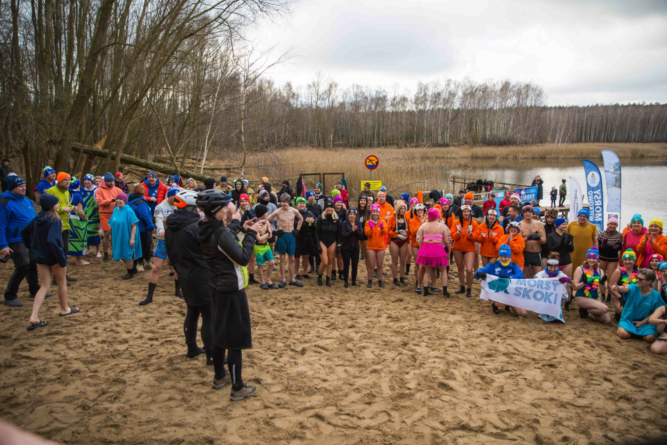 tłum ludzi w strojach kąpielowych robi ćwiczenia na plaży
