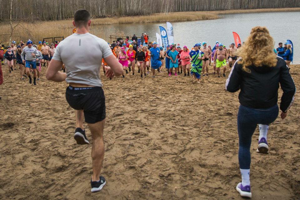 tłum ludzi w strojach kąpielowych robi ćwiczenia na plaży