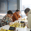 grupa ludzi siedzi przy stolikach i gra w szachy
