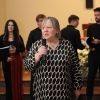 kobieta z mikrofonem, w tle osoby z chóru