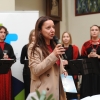 kobieta z mikrofonem, w tle osoby z chóru