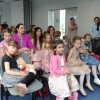 dzieci i dorośli siedzą na krzesłach w sali