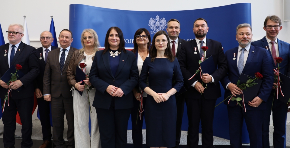 grupa ludzi stojących przy ściance z orłem