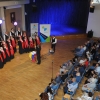 kobiety i mężczyźni śpiewający w chórze na scenie oraz publiczność siedząca na krzesłach - zdjęcie od góry