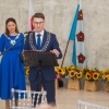 mężczyzna mówi do mikrofonu, za nim stoi kobieta, w tle flaga gminy Murowana Goślina