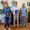 3 mężczyzn stoi przy ścianie z godłem i herbem Murowanej Gośliny