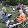 grupa osób siedzi na leżakach i słucha opowieści kobiety, która siedzi przed nimi