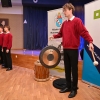 Chórzysta grający na instrumencie perkusyjnym, w tle inni chórzyści.