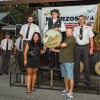 trzy osoby na podium, dwie osoby pod podium trzymają tarczę