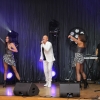 Mężczyzna z mikrofonem, dwie tancerki oraz DJ na scenie.