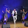 Mężczyzna z mikrofonem, dwie tancerki oraz DJ na scenie.