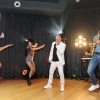 Artysta z mikrofonem, dwie tancerki, muzyk grający na saksofonie oraz DJ na scenie.