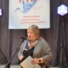 Kobieta z mikrofonem, baner festiwalowy w tle.