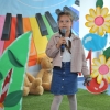 11. Na tle kolorowej scenografii stoi dziewczynka z warkoczykami z mikrofonem w ręku.