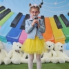 Na tle kolorowej scenografii dziewczynka śpiewa do mikrofonu