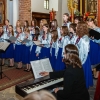 chór dziewczęcy z dyrygentką przed ołtarzem, po boku kobieta akompaniująca na instrumencie klawiszowym