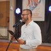 Mężczyzna przy mikrofonie, baner festiwalowy w tle.