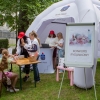 stoisko banku, przy stole siedzą dwie dziewczynki i stoją dwie kobiety, wewnątrz namiotu stoją dwie inne kobiety